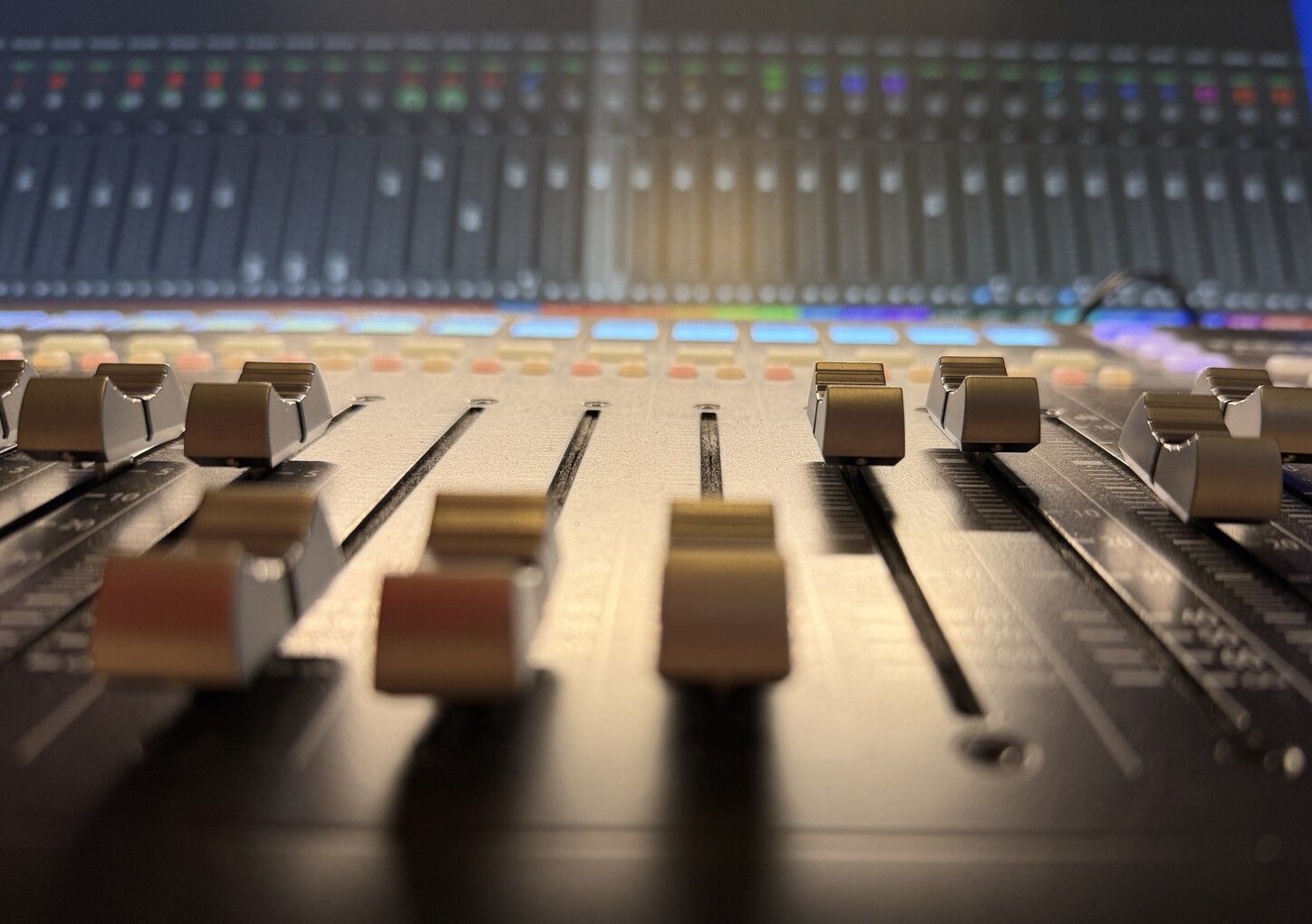 Close view across the faders of a mixing console in Jamie Penner’s studio, lit in warm light